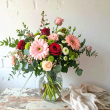 Bouquet of pink and white roses, pink gerbera daisies, and commercial mums with fresh seasonal greenery, arranged in a soft and cheerful style.