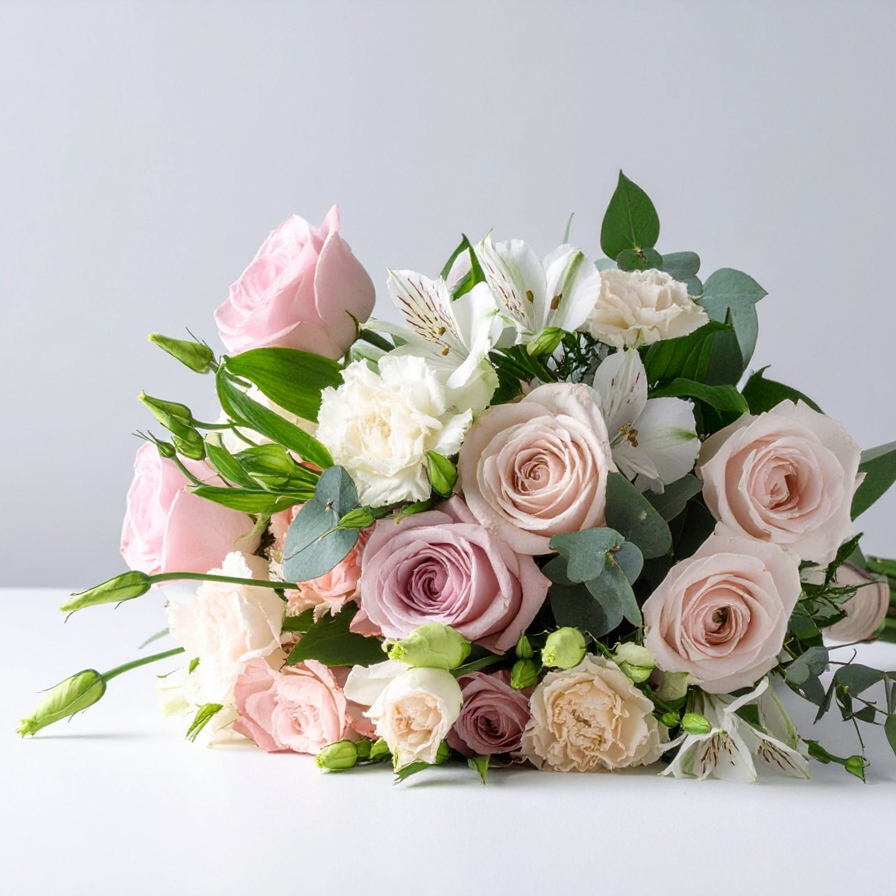 Bouquet of pink and white roses, pink gerbera daisies, and commercial mums with fresh seasonal greenery, arranged in a soft and cheerful style.
