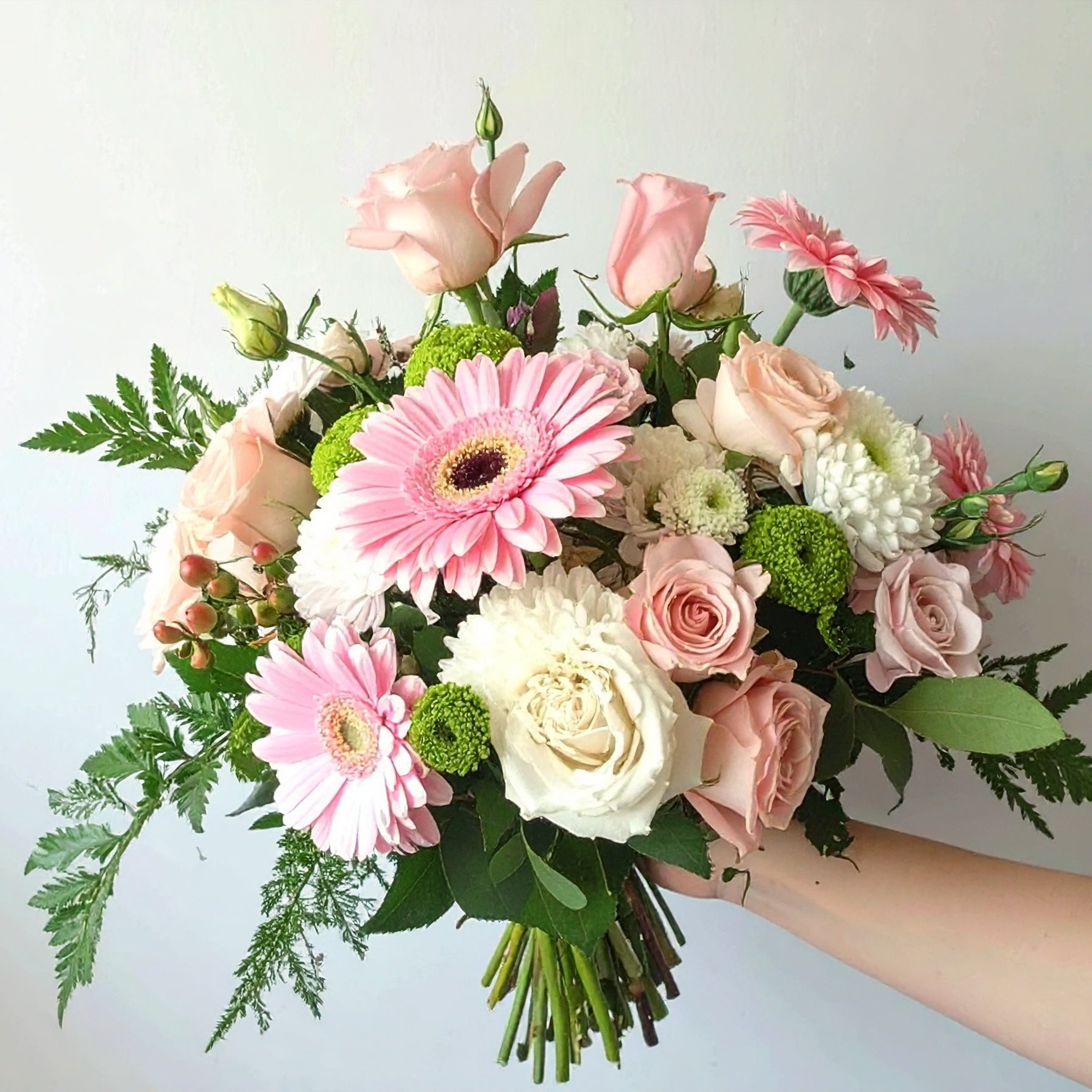 A pastel floral arrangement with blush roses, white flowers, stock, alstroemeria, and greenery in soft tones of pink, white, and green.