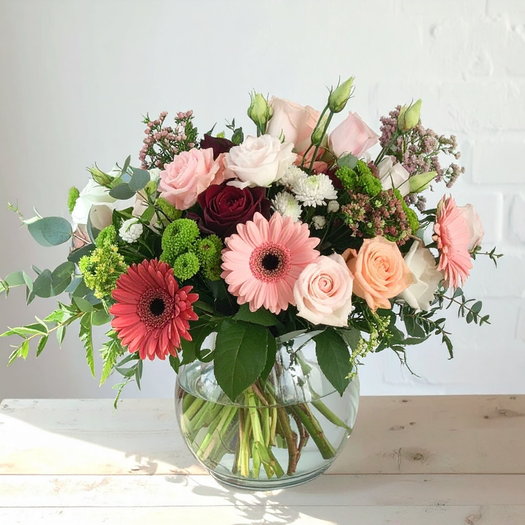The Creemore Flower Company elegant pastel bouquet with blush roses, white hydrangeas, stock, alstroemeria, and greenery in a clear glass vase.